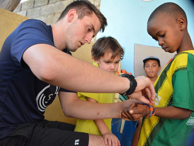 male college student helps African boy with bracelet